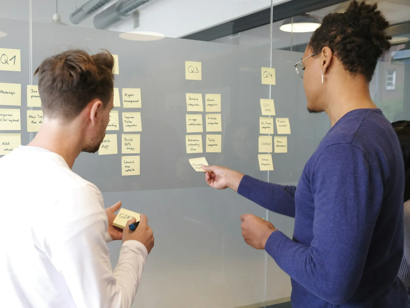 Dos personas planean un proyecto con notas adhesivas en una pared de vidrio